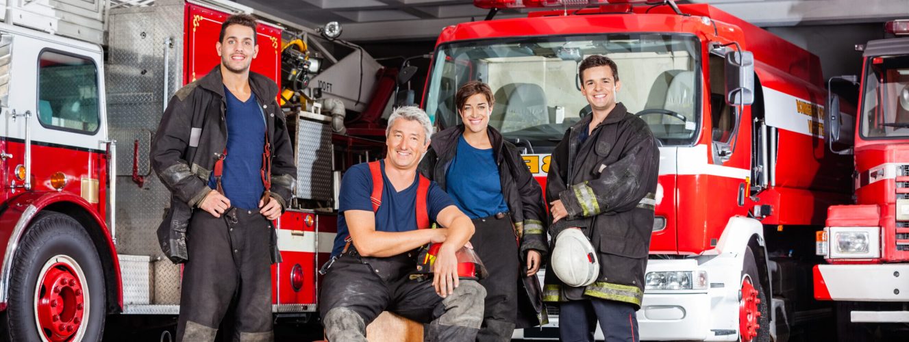 Firefighter Team A group of safe and strong firefighters in the station with firetrucks behind them