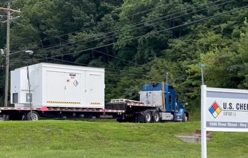 White, dual room chemical storage building on tractor trailer truck with US Chemical Storage sign in the foreground